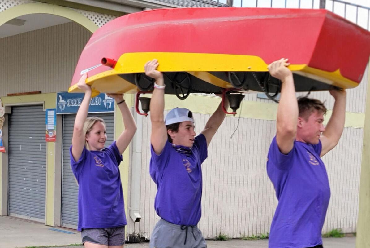 在一次社区服务郊游中，两名男学生和一名女学生将一艘船举过头顶，穿过埃尔德里奇公园